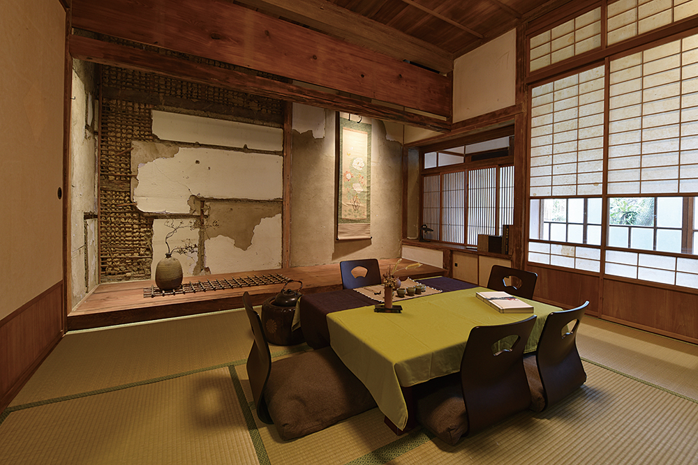 原客廳改成的茶室，可容納8人。斑駁牆面的左半邊可見過往安裝櫃子的痕跡。右半邊的掛軸則是平常就很愛蒐古物的陳勤忠自己的收藏。