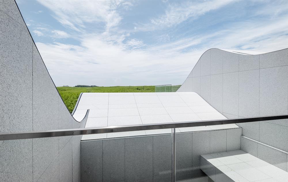 三樓祠堂陽台的景色向外延伸，穿越中庭及捲脊地景，前方綠蔭和遠方海景一覽無遺。