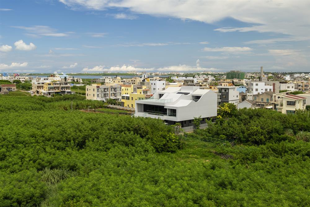 順著南北向的紋理，澎湖厝由三個擁有各自獨特的捲脊屋頂輪廓構成；白色石材的外牆與藍天綠地形成強烈對比。