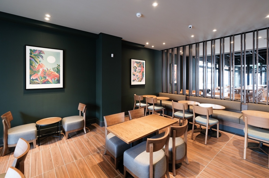 小檔星巴克小港中安後區空間則以綠色牆面搭配海洋波浪及鱗片的意象彩繪呈現，透過鏤空格柵分割區域，創造出明快活潑而清爽的空間，提供給顧客旅途中舒適的休息空間。