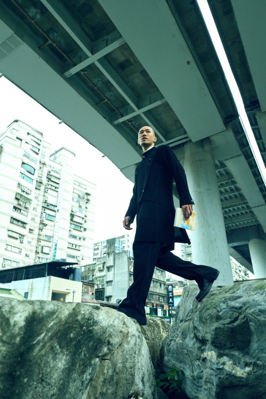 someshiit山姆身著Painter's Gear 吊帶背心、Tailored Pleats 1 無領長外套、Streamline Shirt 變化領巾襯衫、Pleats Bottoms 1 內開衩直筒褲 all by HOMME PLISSÉ ISSEY MIYAKE（攝影：林科呈）