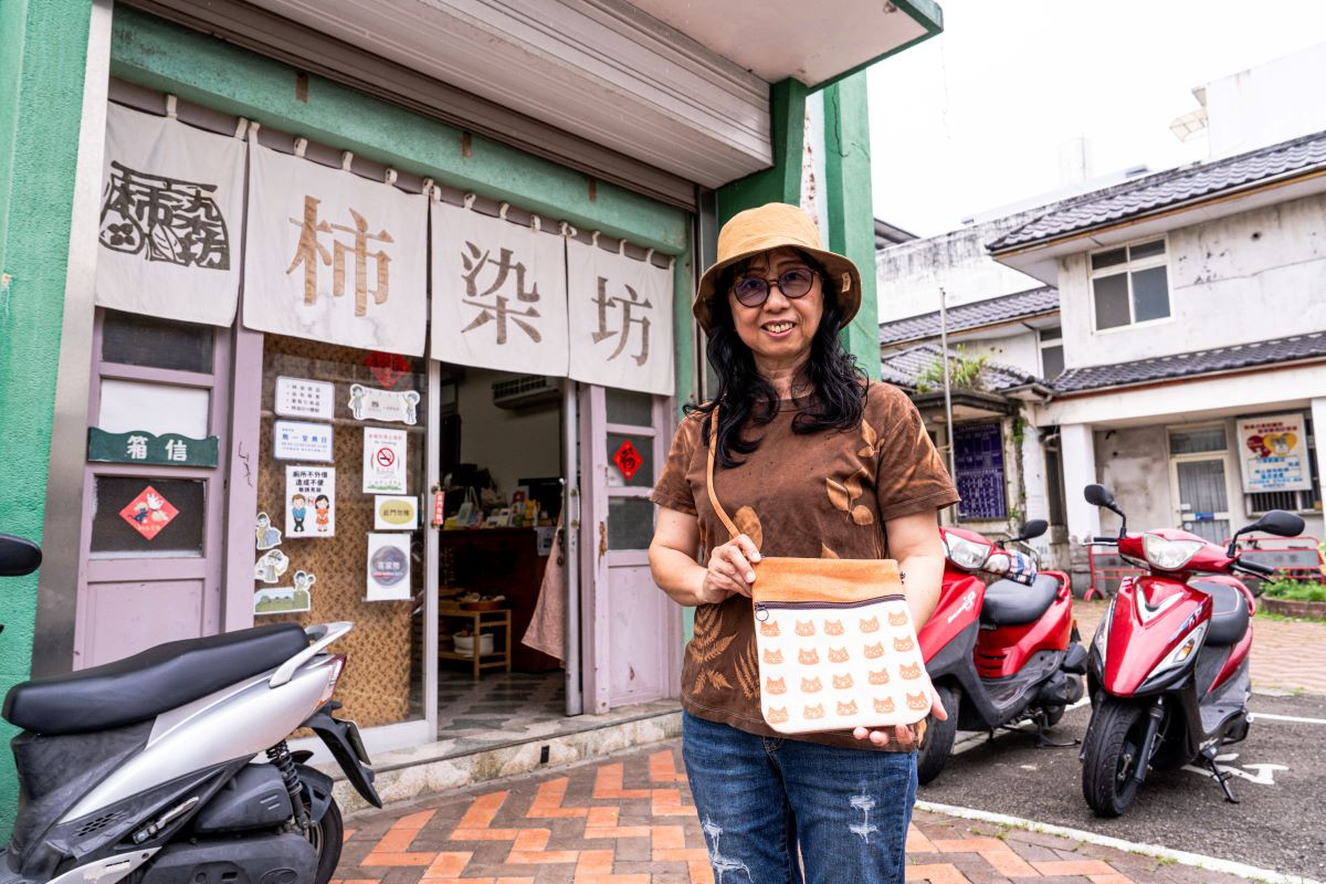站在新埔柿染坊前，總幹事鍾夢娟與她手中的柿染作品。這座染坊不僅是工藝傳承的基地，更是推動傳統技藝走向當代生活的重要推手。（圖片來源：《生活工藝誌》第十四期）